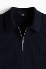 Remera polo de manga corta color azul marino en punto acanalado de mezcla de algodón con cuello y medio cierre. Remate acanalado de raya fina en mangas y bajo. Corte ajustado que realza el contorno del cuerpo creando una silueta entallada.