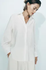Camisa marrón de corte holgado, con cuello de solapa, manga larga con pliegues y bajo asimétrico. Cierre frontal con botones.