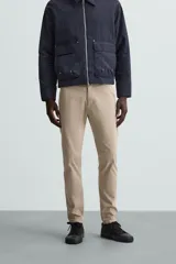 Pantalón chino color beige, corte skinny fit, confeccionado en tejido con mezcla de algodón y elasticidad. Cuenta con bolsillos frontales y traseros. Cierre frontal con cremallera y botón.
