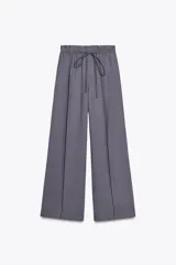 Pantalón gris de tejido fluido, tiro alto con cintura tipo paper bag, bolsillos laterales y cinturón lazada en el mismo tejido.