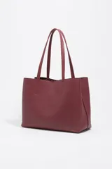 Bolso shopper de piel color borgoña, con textura granulada, asas de hombro y cierre de cordón. Presenta el logo metálico de Bimba y Lola en el frente.