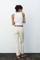 Pantalón de jean color crudo, de tiro alto, corte recto y largo tobillero. Tiene cinco bolsillos, cierre frontal con cremallera y botón metálico.