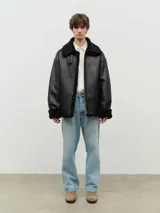 Chaqueta negra de cuero vegano con forro de sherpa, solapas con hebillas, cuello italiano, cierre de cremallera y mangas con puños.