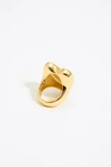 Anillo de metal dorado con forma de corazón, adornado con brillo rojo.