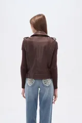 Chaleco estilo biker de eco-cuero color marrón oscuro, con solapas anchas, cierre frontal asimétrico y detalles de tachas plateadas. Presenta cinturón ajustable con hebilla en el ruedo.