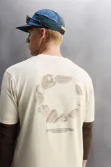Camiseta color crema de corte holgado, cuello redondo y manga corta. Presenta un pequeño estampado con texto en el lado izquierdo del pecho.