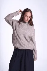 Sweater color beige de tejido de punto con cuello alto y mangas largas. Presenta detalles de ochos en diagonal en los laterales.