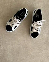 Zapatillas deportivas urbanas con capellada negra, detalles en beige y suela blanca.