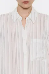 Camisa larga de viscosa con textura, de corte recto, con cuello camisero, manga larga de puño con botón y cierre frontal con abotonadura. Presenta bolsillo de plastrón en el pecho y nudo decorativo en la parte trasera para dar volumen.