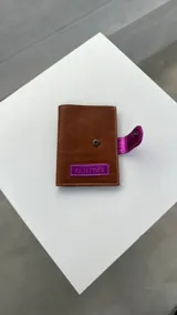 Porta pasaporte marrón con apliques plateados y cierre con broche.