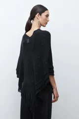 Capa tejida color negro, con cuello redondo, diseño de punto y detalles de lentejuelas. Presenta flecos en el dobladillo.