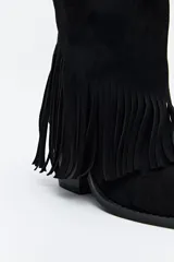 Bota texana de caña alta color beige confeccionada en gamuza, con punta fina, taco cuadrado de madera y detalle de flecos laterales. 