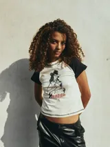 Remera corta color blanco con mangas cortas raglán negras y estampado frontal de una vaquera con la palabra 'Bandida' en rojo.