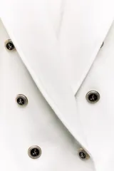 Blazer color blanco hueso, de corte entallado y doble botonadura dorada. Tiene cuello con solapa, mangas largas con hombreras y bolsillos delanteros con solapa.