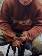 Sweater marrón de tejido de punto con cuello redondo y mangas largas. Presenta un diseño gráfico en color beige en el frente.