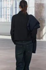 Chaqueta corta negra de cuello solapa y manga larga con puños. Tiene bolsillos de parche en el frente y cierre frontal con botones.