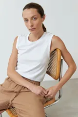 Musculosa blanca de algodón con cuello redondo y detalle de botones dorados en los hombros.