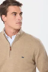 Buzo tejido de lana color beige, con medio cierre metálico y cuello alto. Tiene un pequeño logo bordado en el pecho.