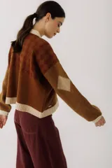 Cardigan color beige con diseño de rombos en blanco, largo a la cintura, con botones en carey y mangas largas.