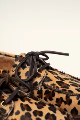 Mocasín tipo boat shoe con estampado de vaca en tonos marrón y blanco, confeccionado en cuero. Cuenta con cordones de cuero marrón oscuro y suela de goma.