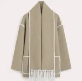 Conjunto de saco y bufanda color gris oscuro con detalles de costura en blanco. El saco es de corte holgado, con cuello alto, cierre frontal con botones, bolsillos frontales y mangas largas. La bufanda es larga y con flecos.