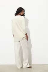 Chaqueta color crema de punto con cuello redondo y manga larga. Tiene bolsillos delanteros de plastrón, pespuntes combinados a contraste y cierre frontal con botones dorados.