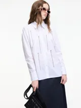 Camisa blanca de algodón con cuello camisero, cierre frontal con botones y apliques de cadenas plateadas.