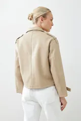 Chaqueta corta color beige de cuero sintético, con cuello alto, cierre frontal con botones a presión y bolsillos laterales con solapa.