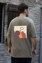 Remera color arena con estampa en la espalda de un paisaje con montañas, sol y una figura humana. Corte clásico y mangas cortas.