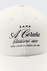 Gorra de béisbol negra de Zara con bordado frontal en blanco que dice "A Coruña Established 1975 Rúa Juan Flórez 64-66".