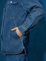 Sobrecamisa de denim azul con cuello camisero, cierre frontal con botones a presión, mangas largas con puños abotonados, dos bolsillos con solapa abotonada en el pecho y corte recto.