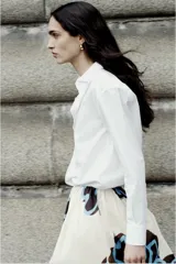 Camisa blanca de algodón con cuello solapa, manga larga con puños y cierre frontal con botones.