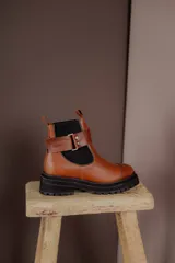 Botas de cuero color marrón oscuro, estilo Chelsea, con elástico lateral negro y suela track negra. Incluye correa de cuero desmontable con hebilla.