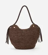 Bolso de playa tipo canasta, tejido en fibra de papel color marrón oscuro, con forma redondeada y abertura superior curva. Cuenta con asas trenzadas de material sintético marrón oscuro y detalles de flecos colgantes a los lados.