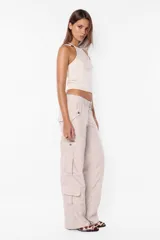 Pantalón cargo color arena de corte recto y tiro bajo, con recortes y presillas dobles en la cintura. Tiene acceso mediante cierre de nylon y botón personalizado, seis bolsillos laterales y dos en la espalda con tapa y botón snap a presión.