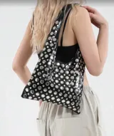 Bolso tipo tote de cuero sintético color borgoña, con apliques metálicos plateados y asa corta.