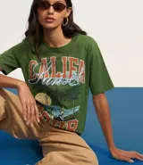 Remera verde militar de algodón con cuello redondo y mangas cortas. Estampado frontal con palmeras, olas y texto "Califa Hour".