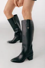Bota bucanera de cuero color marrón, con caña alta, punta fina y taco cuadrado. Presenta detalle de costuras verticales en la caña y cierre lateral.