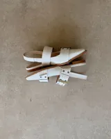 Chatas de cuero vacuno color blanco con textura tipo piel de cocodrilo, punta fina, dos tiras anchas sobre el empeine con hebillas metálicas y tira trasera con hebilla.