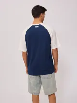 Remera azul marino con mangas raglán color crema y estampado frontal con el logo de Rusty en blanco.