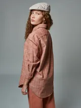 Camisa de manga larga color ladrillo con rayas blancas, confeccionada en lino. Tiene cuello clásico, cierre frontal con botones y bolsillo de parche en el pecho.