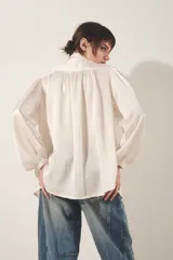 Camisa color blanco hueso de corte fluido, con cuello camisero, mangas largas abullonadas con puño abotonado y detalle de frunces.