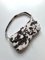 Cartera baguette con estampado de vaca en tonos blanco y marrón.