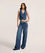 Pantalón de jeans azul de corte wide leg, tiro medio, con cintura de diseño traspasado y cierre tradicional.