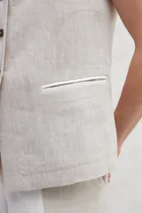 Chaleco color crema de lino, con cuello mao, cierre frontal con botones y bolsillos ojal a contratono.