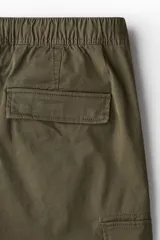 Pantalón cargo color verde oliva, de corte slim fit, con cintura elástica ajustable con cordón, bolsillos laterales al bies y bolsillos cargo con solapa y botón a presión en los muslos.