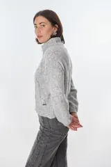 Cardigan color crudo de tejido de punto con diseño trenzado, cuello alto y cierre frontal con cremallera.