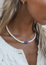 Collar corto de cuentas de caracol blancas con un dije central de cerámica azul en forma de pez.