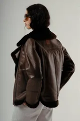 Chaqueta estilo aviador o biker de cuero marrón oscuro con forro y cuello de piel sintética negra. Presenta cierre asimétrico frontal y bolsillos laterales con cierre.