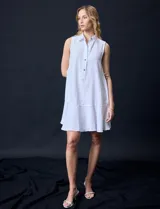 Vestido corto blanco de gasa, sin mangas, con cuello camisero, abertura central con botones y terminación de ruedo con volado.